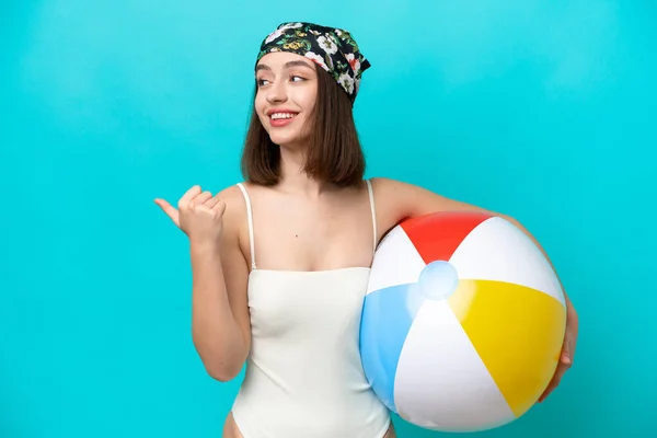 Young Ukrainian Woman Holding Beach Ball Isolated Blue Background Pointing — стокове фото
