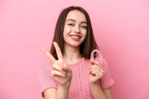 Młoda Ukraińska Kobieta Trzyma Niewidzialne Aparaty Różowym Tle Uśmiechając Się — Zdjęcie stockowe