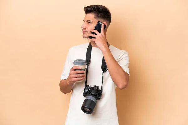 Giovane Fotografo Caucasico Isolato Sfondo Beige Con Caffè Portare Cellulare — Foto Stock