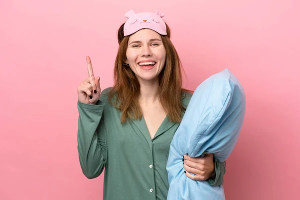 Young English woman in pajamas isolated on pink background in pajamas and pointing up a great idea