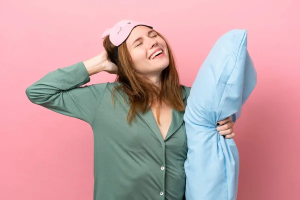 Young English woman in pajamas isolated on pink background in pajamas and holding a pillow and yawning