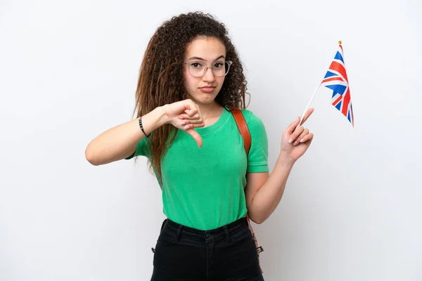 Young Arab woman holding an United Kingdom flag isolated on white background showing thumb down with negative expression