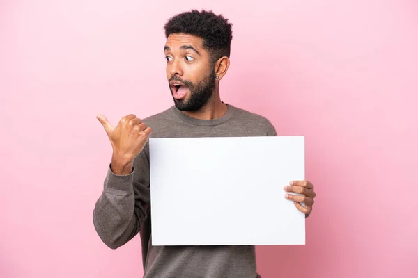 Jovem Brasileiro Isolado Fundo Rosa Segurando Cartaz Vazio Apontando Lado — Fotografia de Stock