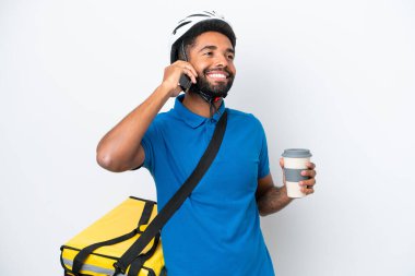 Termal sırt çantalı genç Brezilyalı adam beyaz arka planda izole edilmiş. Elinde kahve ve cep telefonu var.