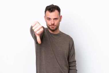 Beyaz arka planda izole edilmiş genç Brezilyalı adam olumsuz ifadeyle baş parmağını aşağı gösteriyor.