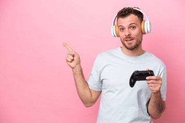 Pembe arka planda izole edilmiş bilgisayar oyunu denetleyicisiyle oynayan genç Brezilyalı adam parmak kenarı işaret ediyor.