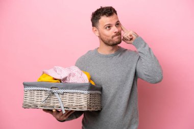 Genç Brezilyalı bir adam pembe arka planda soyutlanmış bir çamaşır sepetini tutuyor. Şüpheleri var ve düşünüyor.