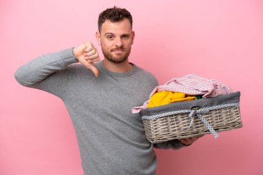 Genç Brezilyalı bir adam pembe arka planda izole edilmiş bir çamaşır sepetini tutuyor.