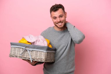 Genç Brezilyalı bir adam pembe arka planda izole edilmiş bir sepet tutuyor gülüyor.