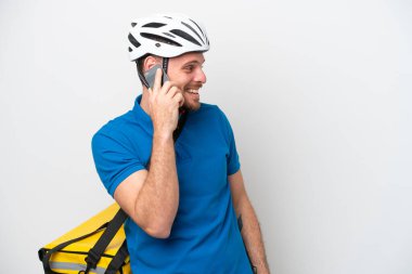 Beyaz arka planda izole edilmiş termal sırt çantalı genç Brezilyalı bir adam cep telefonuyla sohbet ediyor.