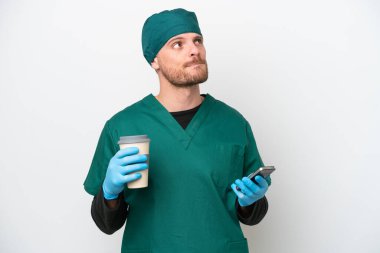 Cerrah Brezilyalı yeşil üniformalı adam beyaz arka planda izole edilmiş. Elinde kahve ve bir şeyler düşünürken cep telefonu var.