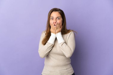 Mor arka planda izole edilmiş orta yaşlı Brezilyalı bir kadın mutlu ve gülümseyen elleriyle ağzını kapatıyor.