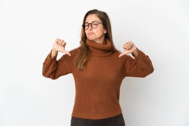 Beyaz arka planda izole edilmiş orta yaşlı Brezilyalı kadın baş parmağını iki eliyle aşağı gösteriyor.