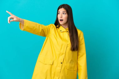 İzole edilmiş mavi arka planda yağmura dayanıklı bir ceket giyen Brezilyalı genç bir kız.