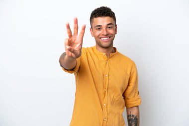 Beyaz arka planda izole edilmiş beyaz Brezilyalı genç adam mutlu ve parmaklarıyla üçe kadar sayıyor.