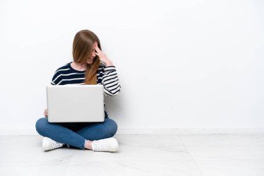 Dizüstü bilgisayarı olan beyaz bir kadın beyaz arka planda izole bir şekilde oturmuş gülüyor.