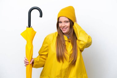 Yağmura dayanıklı paltosu ve şemsiyesi olan beyaz arka planda izole genç beyaz kadın şüpheleri var.