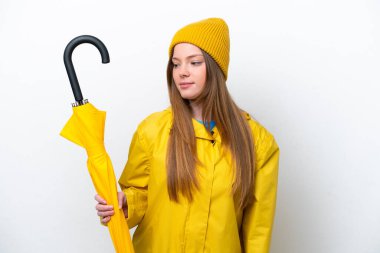 Beyaz arka planda izole edilmiş yağmurluk ve şemsiyeli beyaz kadın yan tarafa bakıyor.