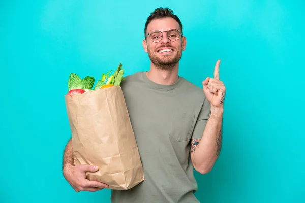 Young Brazilian Man Holding Grocery Shopping Bag Isolated Blue Background — Φωτογραφία Αρχείου