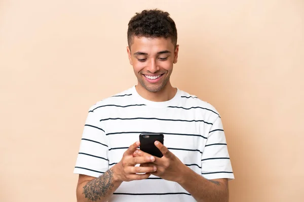 Young Brazilian Man Isolated Beige Background Sending Message Mobile — Zdjęcie stockowe
