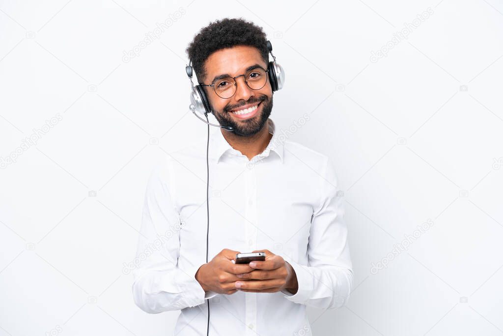Telemarketer Brazilian man working with a headset isolated on white background sending a message with the mobile