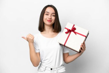 Beyaz arka planda izole edilmiş bir hediye taşıyan genç Ukraynalı kadın bir ürünü sunmak için kenarı işaret ediyor.