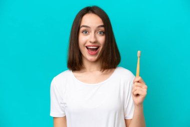 Mavi arka planda diş fırçalayan genç Ukraynalı kadın şaşırmış ve şok olmuş yüz ifadesi ile izole edilmiş.