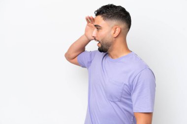 Genç Arap yakışıklı adam beyaz arka planda izole edilmiş. Sürpriz bir ifadeyle yan yana bakarken.