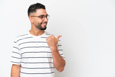 Beyaz arka planda izole edilmiş genç bir Arap yakışıklı bir ürünü sunmak için kenarı işaret ediyor.