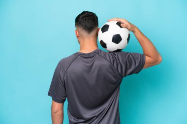 Genç Arap yakışıklı adam mavi arka planda futbol topuyla izole edilmiş.