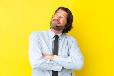 Tele pazarlamacı Hollandalı adam sarı arka planda izole edilmiş kulaklıkla çalışıyor gülümserken yukarı bakıyor