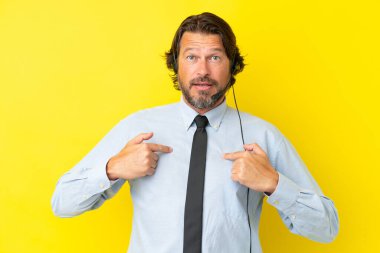 Tele pazarlamacı Hollandalı adam sarı arka planda, şaşırtıcı bir yüz ifadesi olan bir kulaklıkla çalışıyor.