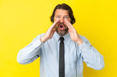 Tele pazarlamacı Hollandalı adam sarı arka planda izole edilmiş bir kulaklıkla çalışıyor bağırıyor ve bir şey duyuruyor.