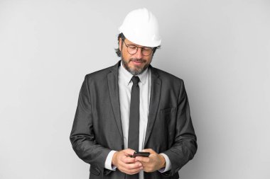 Miğferi izole edilmiş arka planı olan genç mimar cep telefonuyla mesaj gönderiyor.