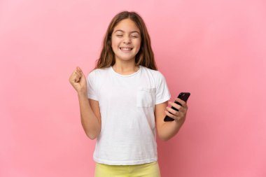 İzole edilmiş pembe arka plan üzerinde cep telefonu kullanan ve zafer hareketi yapan bir çocuk.
