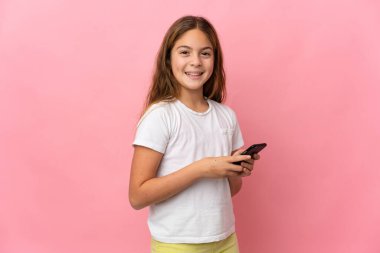 İzole edilmiş pembe arkaplan üzerindeki çocuk cep telefonuyla bir mesaj veya e- posta gönderiyor