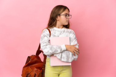 İzole edilmiş pembe arka planı olan öğrenci küçük kız yan tarafa bakıyor.