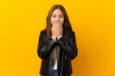 İzole edilmiş sarı arka plandaki çocuk mutlu ve gülümsüyor elleriyle ağzını kapatıyor.