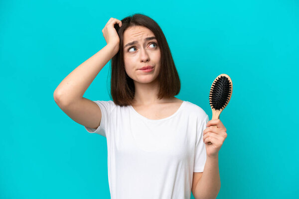 Молодая украинка с расческой для волос изолирована на синем фоне с сомнениями и с запутанным выражением лица