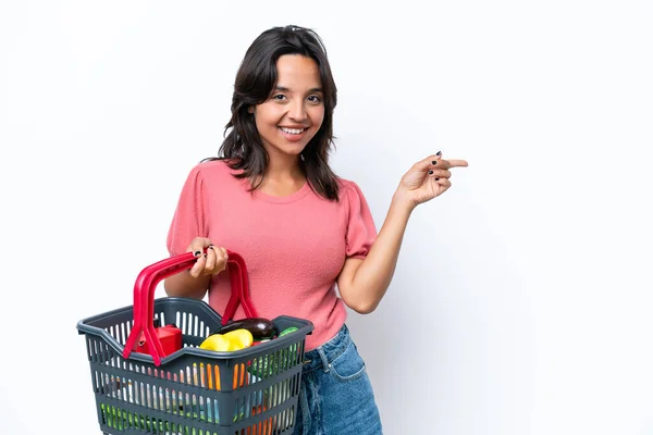 年轻女人拿着一个装满食物的购物篮 手指指向旁边 — 图库照片