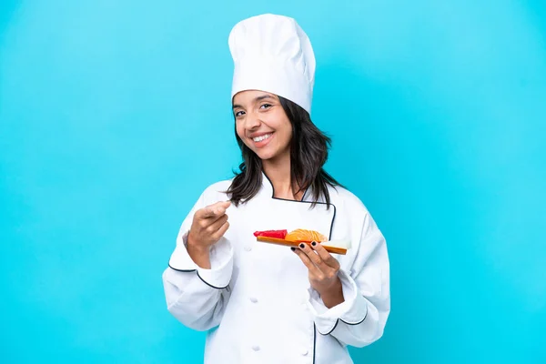 Young hispanic chef woman holding sashimi isolated on blue background pointing front with happy expression