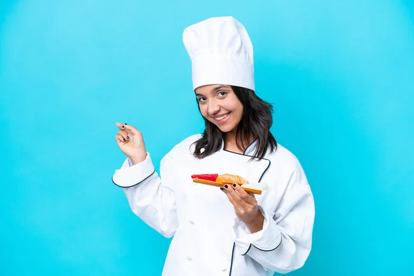 Young hispanic chef woman holding sashimi isolated on blue background pointing back