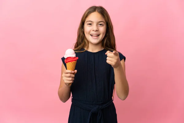 Child with a cornet ice cream over isolated pink background surprised and pointing front