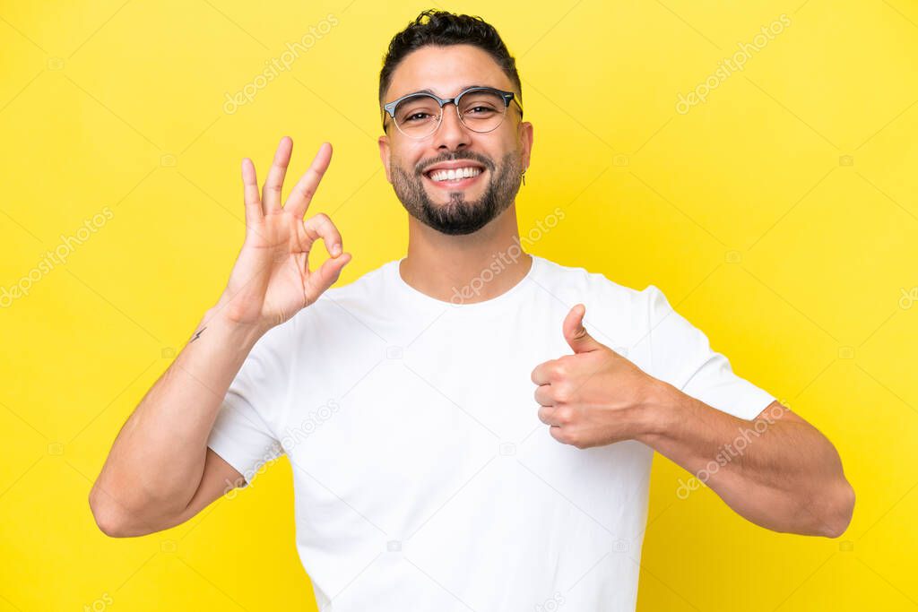 Young Arab handsome man isolated on yellow background With glasses and doing OK sign