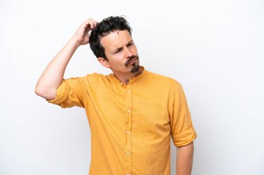 Bıyıklı genç adam beyaz arka planda izole edilmiş. Kafasını kaşırken şüpheleri var.