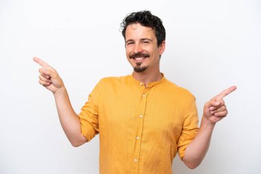 Bıyıklı genç adam beyaz arka planda izole edilmiş, parmak uçlarını işaret ediyor ve mutlu.