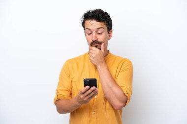 Bıyıklı genç adam beyaz arka planda izole edilmiş düşünüyor ve bir mesaj gönderiyor.