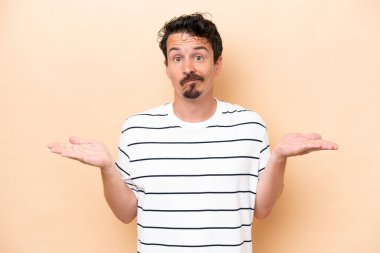 Beyazlı genç bir adam bej arka planda izole edilmiş. El kaldırırken şüphe duyuyor.