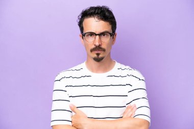 Mor arka planda gözlüklü ve kolları çaprazlanmış genç beyaz bir adam.