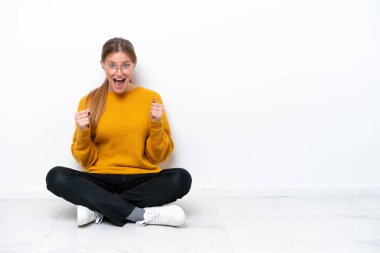 Beyaz arka planda tek başına oturan beyaz tenli genç bir kadın galibiyetini kutluyor.